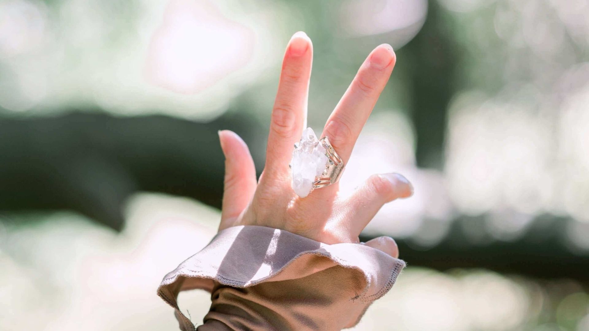 A woman's hand holding a quartz crystal. She's outside in a park or grassy area.