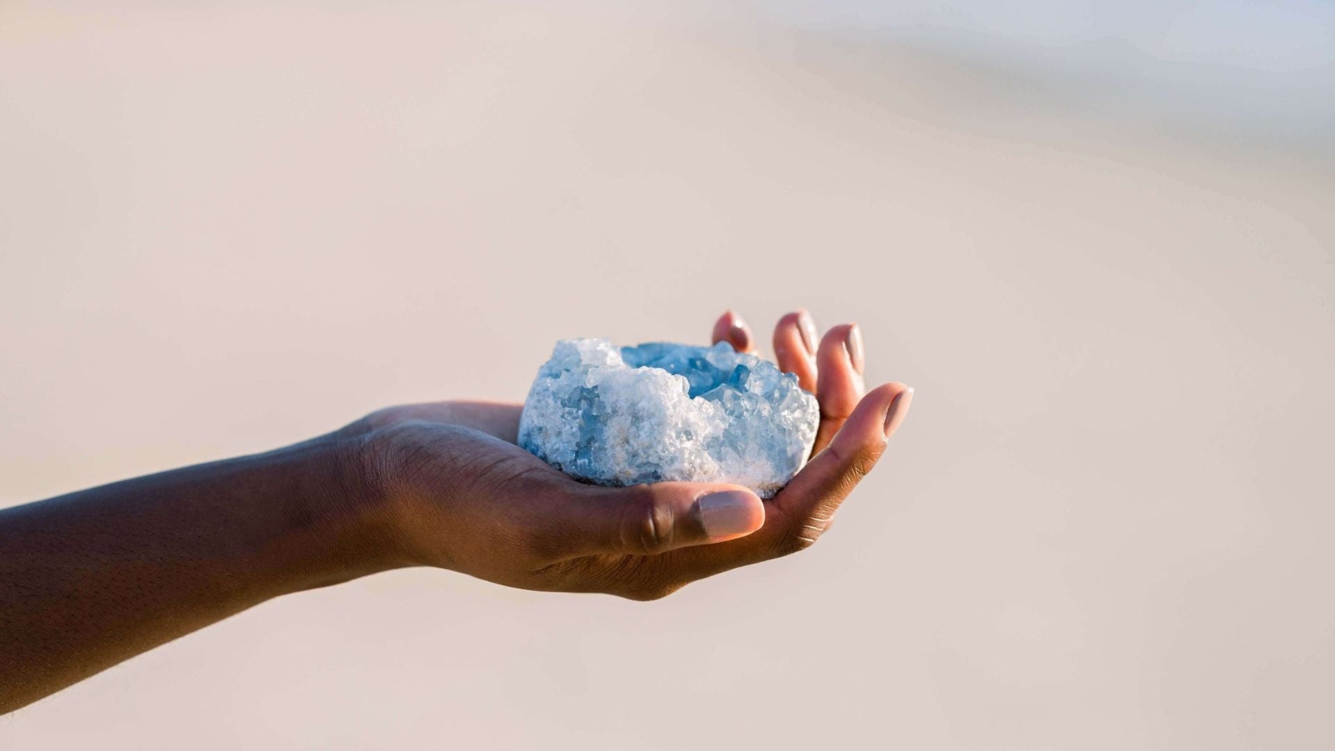 A woman's outstretched arm holding a piece of celestite with the beach in the background