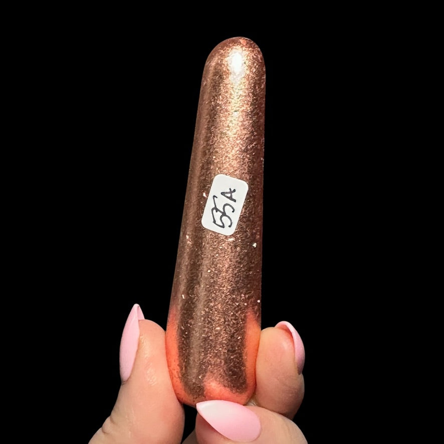 A hand holding a shiny, copper-colored object with a label on it.