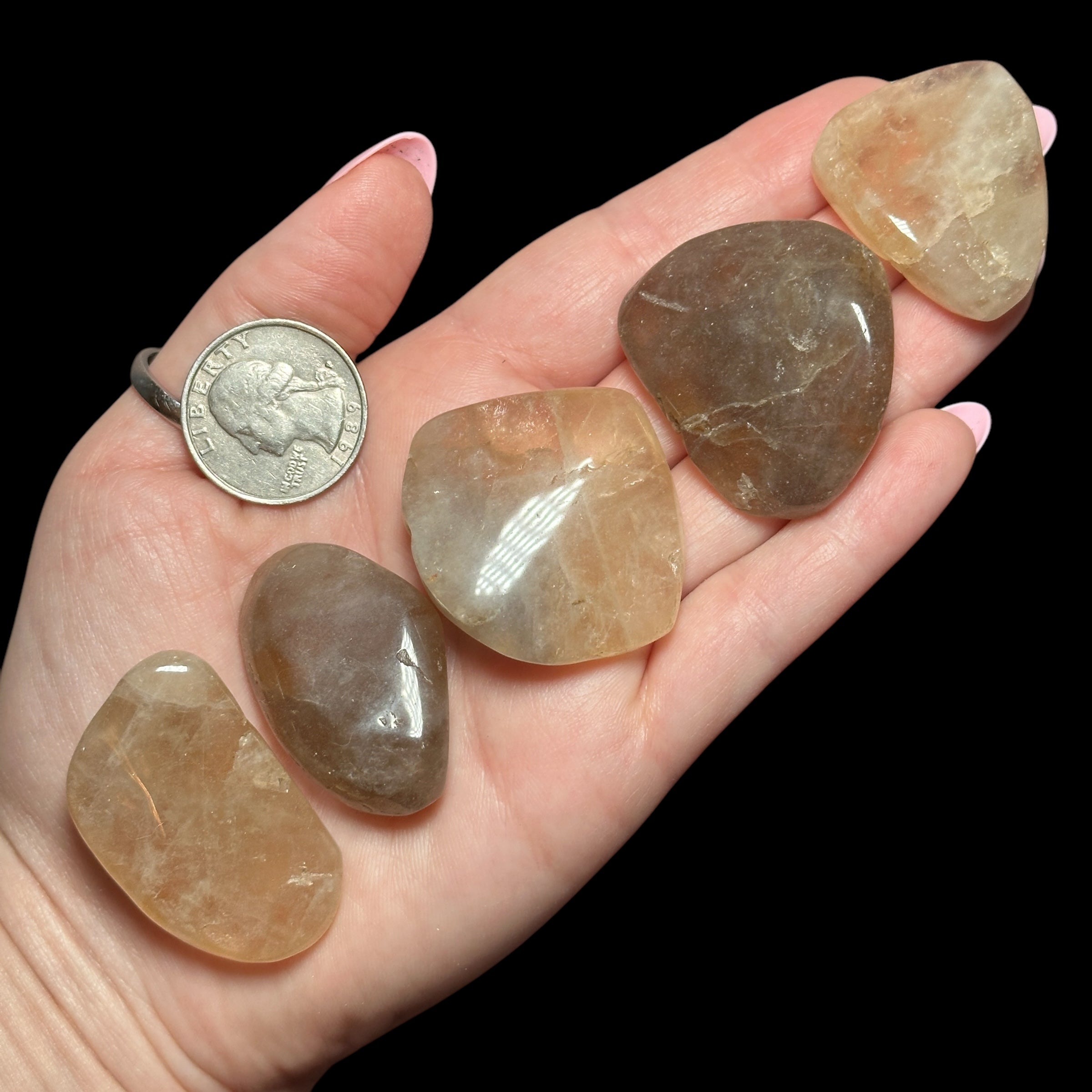 A hand holding five smooth, polished stones in various shades of brown and beige, with a quarter for scale.
