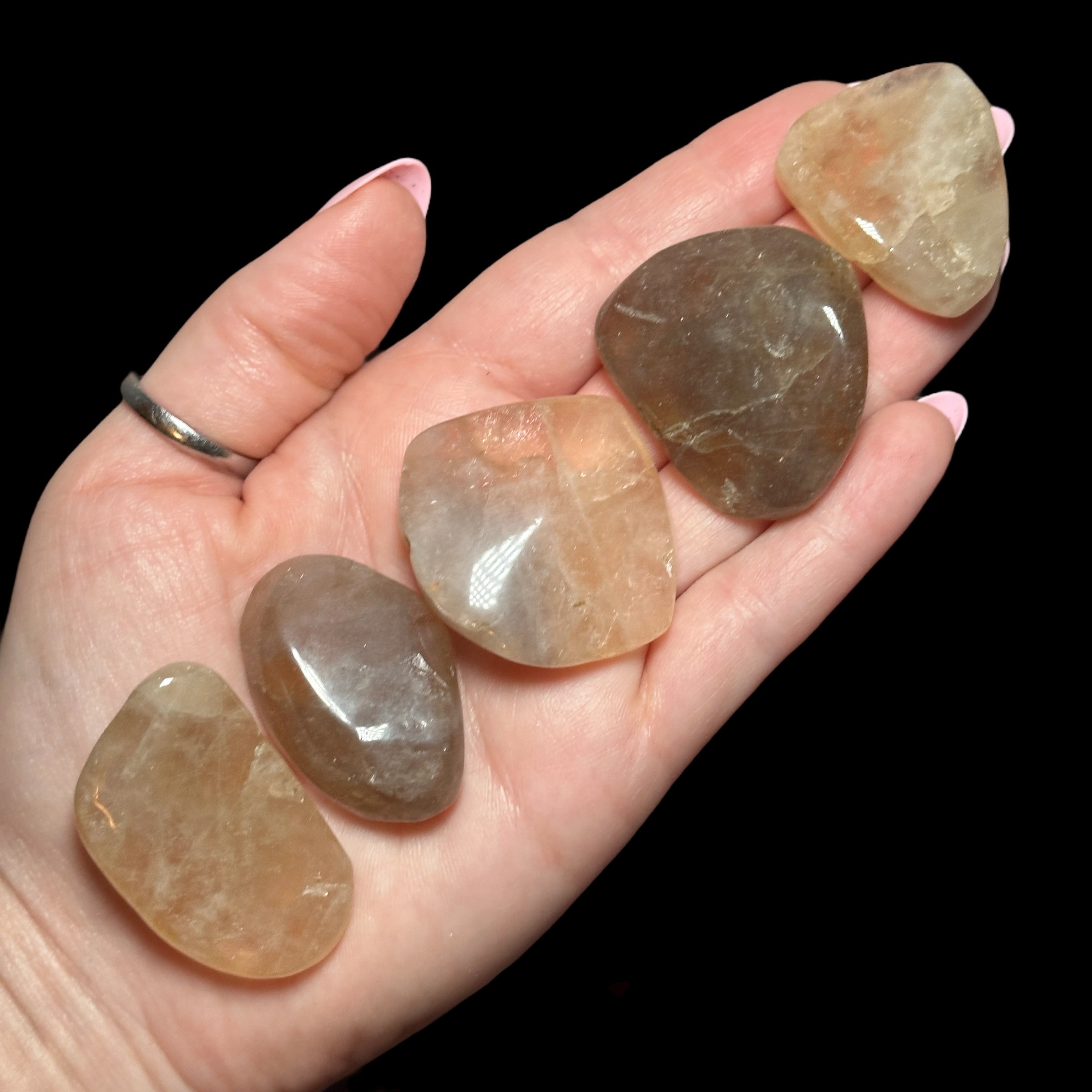 A hand holding five polished stones of varying shapes and colors.