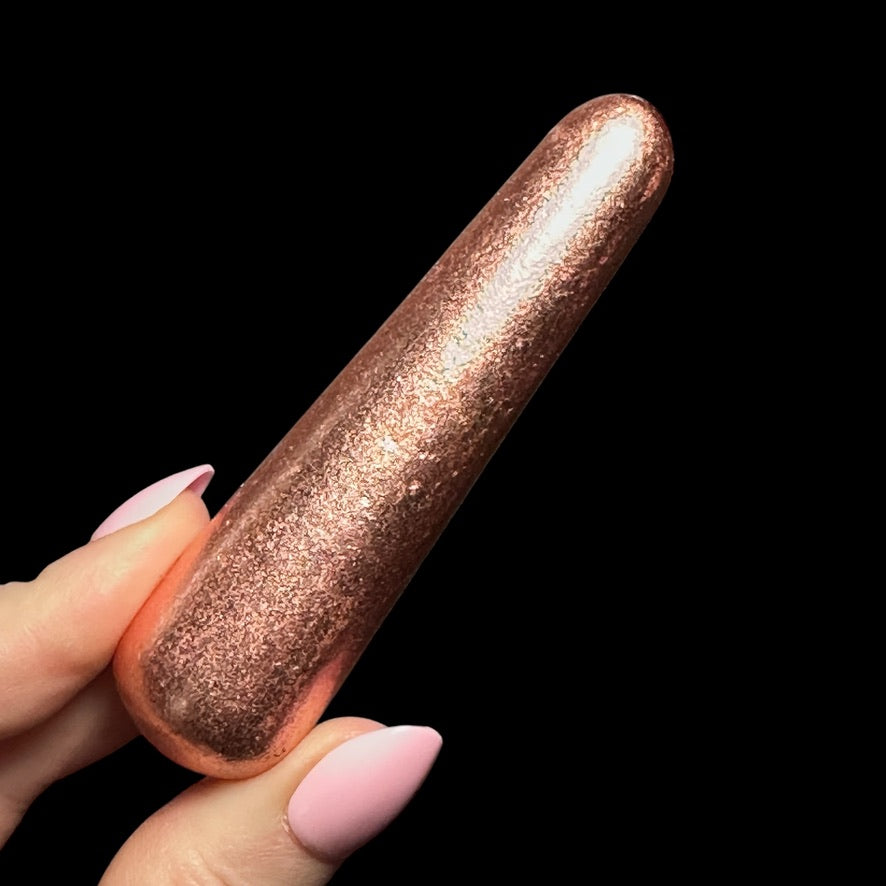 Hand holding a shiny, rose gold glitter nail art tool