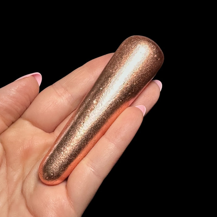 A hand holding a shiny, copper-colored massage tool.