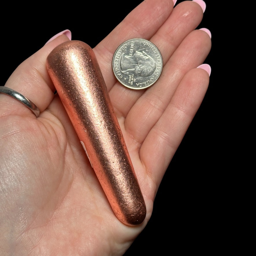 A hand holding a metallic copper-colored object next to a quarter for size comparison.