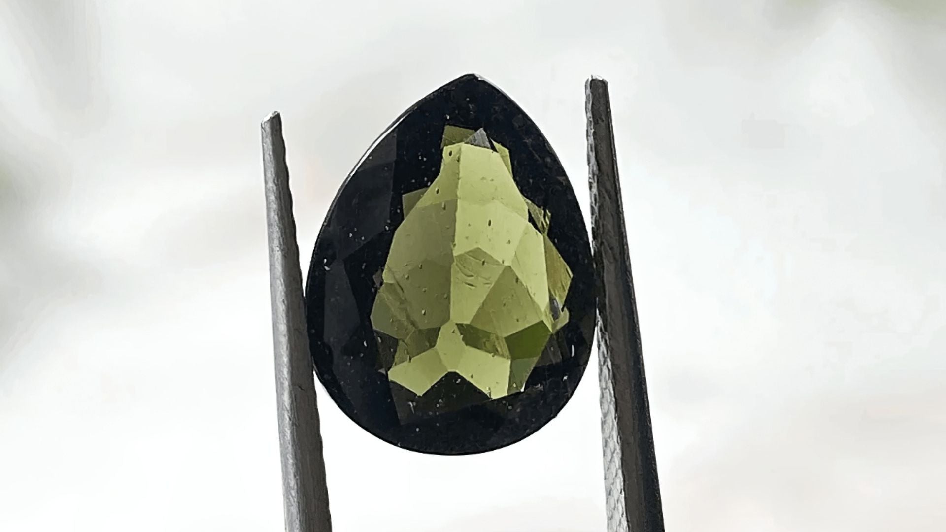 A moldavite teardrop-shaped gem held by tweezers