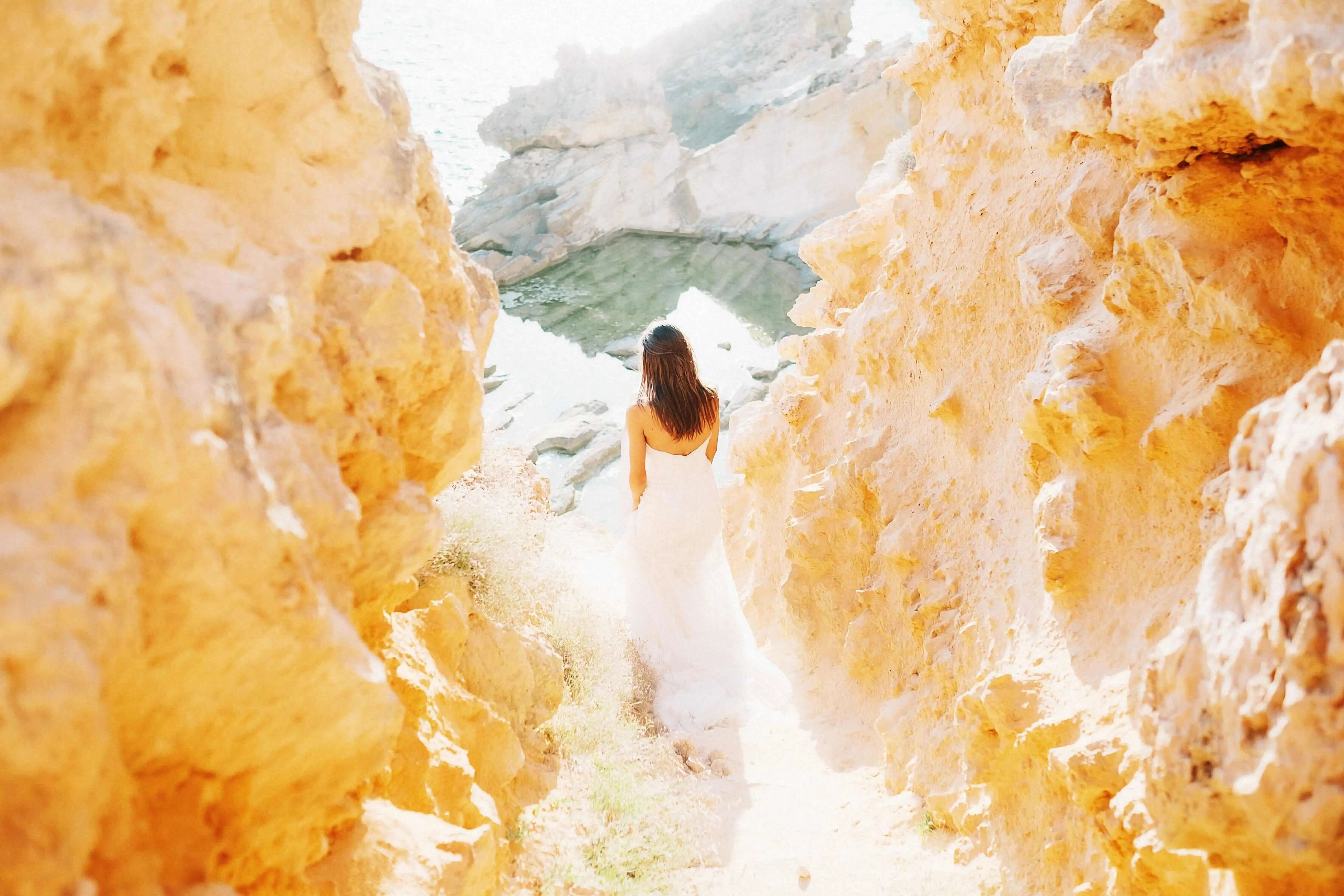 A woman in white walking between two cliffs at the beach on a sunny day