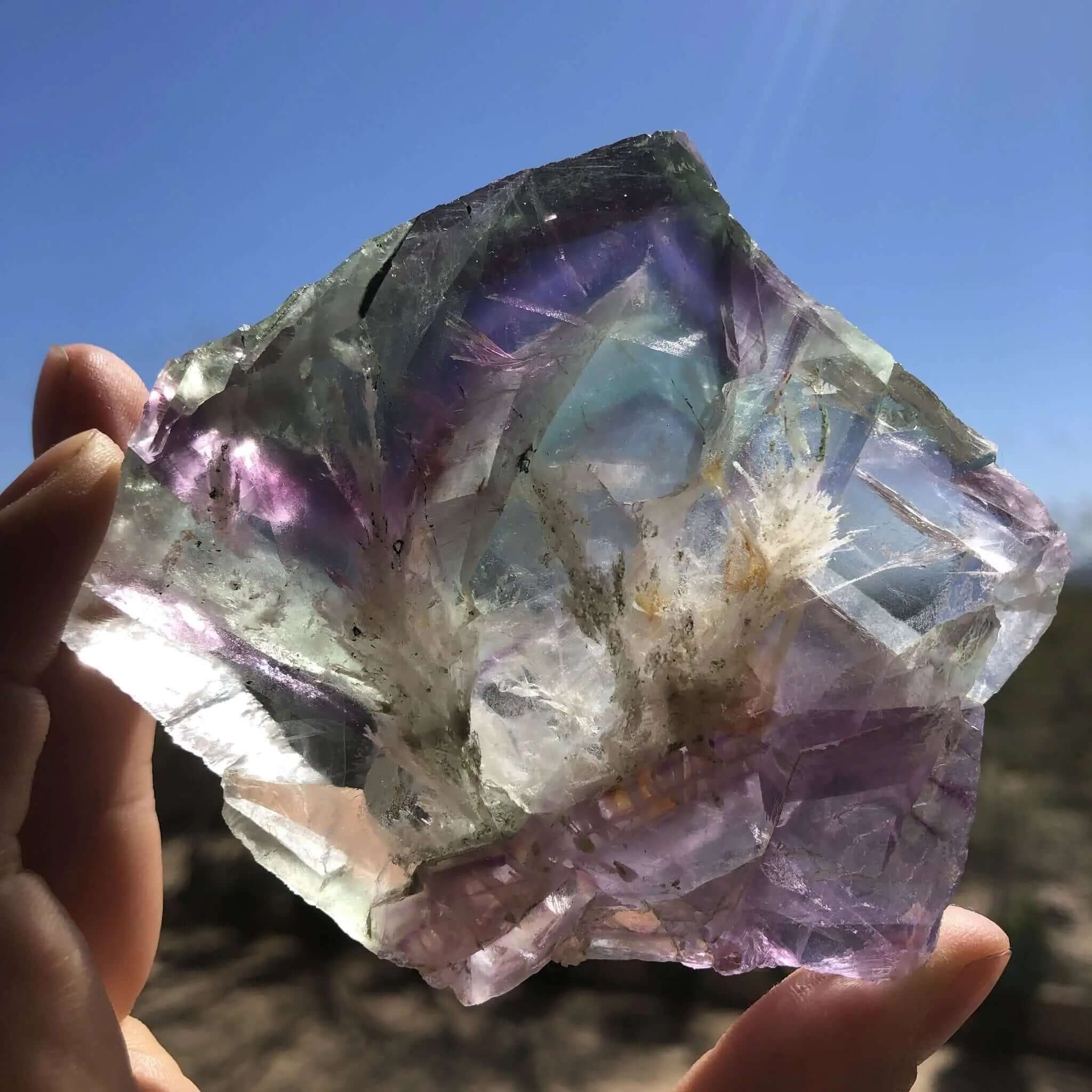Pastel colored fluorite slice held up to the sun with a blue sky in the background